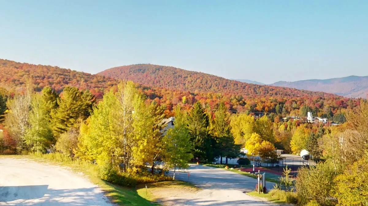 A scenic view of rolling hills, vibrant autumn foliage, and a distant small town, evoking the sense of being close to nature and the mountains.