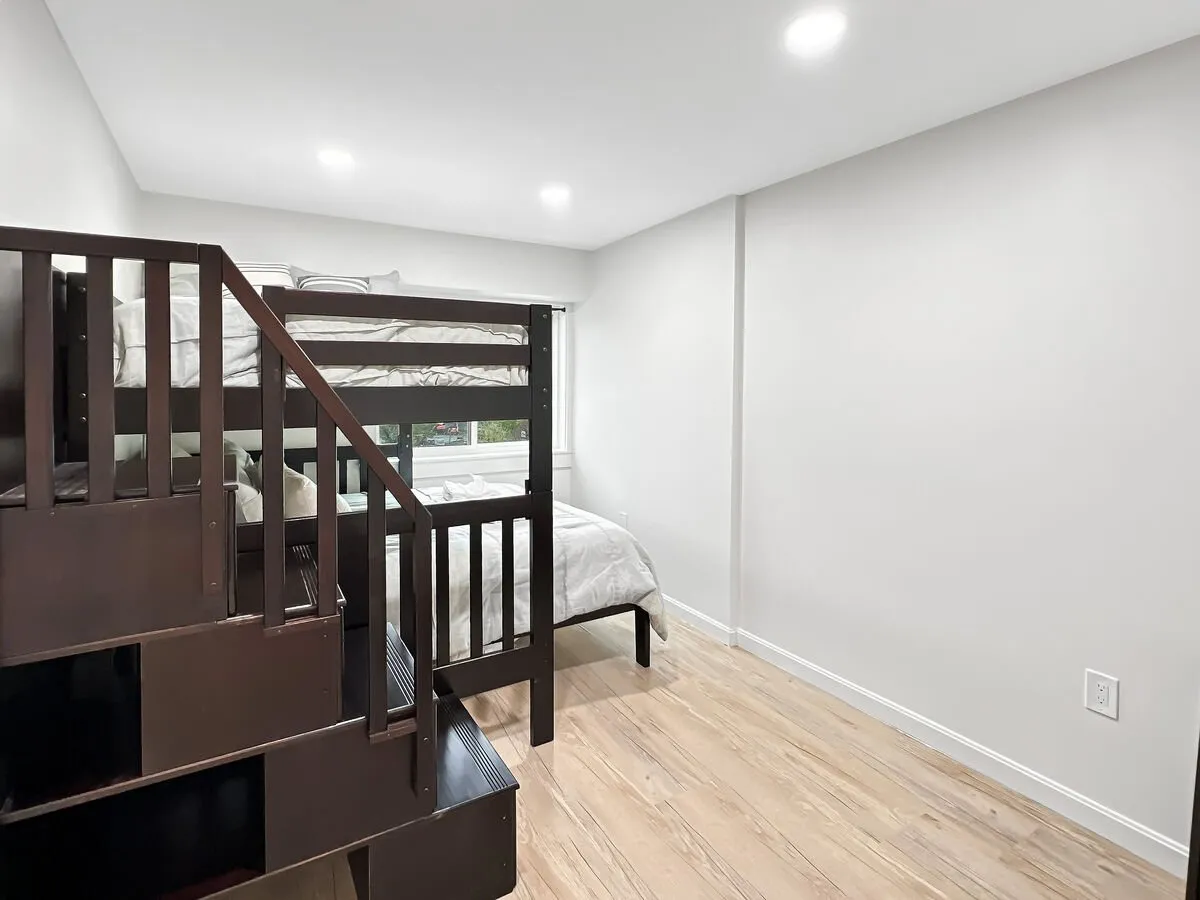 This playful and welcoming bedroom scene highlights a sturdy bunk bed with a staircase and a large window providing ample daylight. The room’s layout promotes relaxation, play, and restful sleep for families or groups, with inviting bedding and clever use of space.