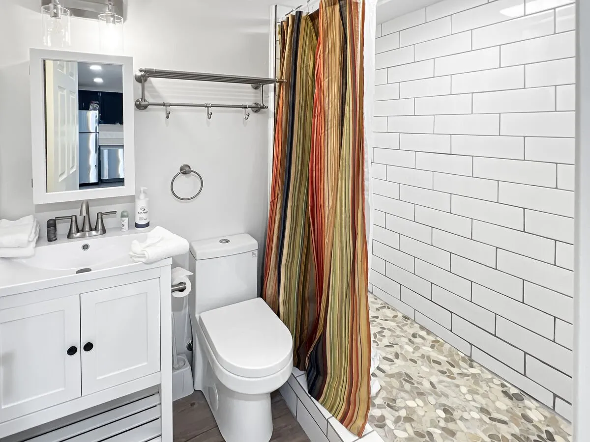 An inviting interior bathroom scene highlights a modern, fresh space with a spacious sink and mirror, a shower with curtain, and decorative flooring. The clean lines and bright ambiance set a spa-like tone, suggesting comfort and relaxation after an active day.